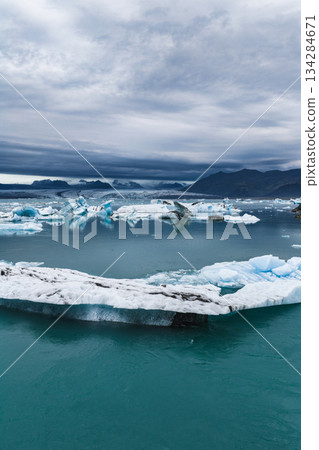 Jokulsarlon Glacier Lagoon in Iceland features turquoise water with floating icebergs, rugged mountains in the background, and an overcast sky. Jokulsarlon Glacier Lagoon in Iceland features turquoise water with floating icebergs, rugged mountains in the background, and an overcast sky. 134284671
