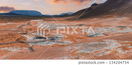 Hverir geothermal area near Lake Myvatn, Iceland, features vibrant orange and yellow earth, steaming fumaroles, bubbling mud pots, and a wooden walkway. 134284734