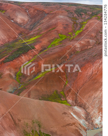 Multicolored hills of Iceland's Rainbow Mountains with red, orange, and green hues. Lush moss contrasts with volcanic terrain and mineral rich slopes. 134284776