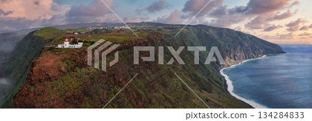 Aerial view shows Miradouro Farol da Ponta do Pargo, Madeira, Portugal, on a sheer cliff above the Atlantic, with beach, fields, pastel light, and long headlands Aerial view shows Miradouro Farol da Ponta do Pargo, Madeira, Portugal, on a sheer cliff above the Atlantic, with beach, fields, pastel light, and long headlands 134284833