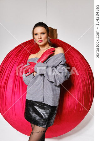 Model poses in front of large red ornament during fashion shoot in studio setting Model poses in front of large red ornament during fashion shoot in studio setting 134284865