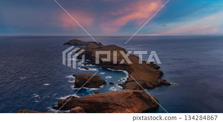 Aerial view of Ponta de Sao Lourenco, Madeira, Portugal at dusk, volcanic cliffs and sea stacks face waves as long exposure smooths water under soft low light 134284867