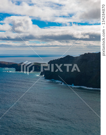Steep volcanic cliffs meet deep blue water at Ponta de Sao Lourenco, Madeira, Portugal. Daytime waves strike serrated headlands under layered clouds, wide angle view. 134284870