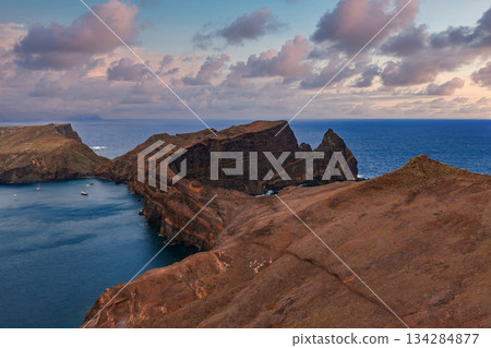 Rugged rust colored cliffs and peninsula form a narrow isthmus and cove at Ponta de Sao Lourenco, Madeira, Portugal. Boats anchor as soft late day light defines rock 134284877