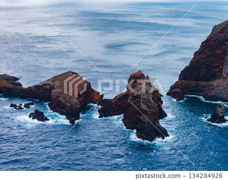 Jagged volcanic sea stacks and rock arches rise from the Atlantic at Ponta de Sao Lourenco, Madeira, Portugal, with white surf and diffused light from an overcast day. 134284926