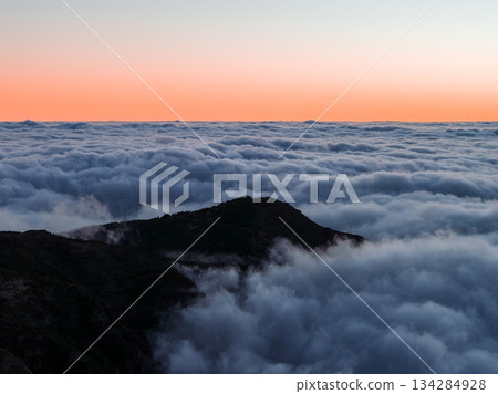 A mountain ridge rises above a sea of clouds at sunrise in Madeira, Portugal, near Pico do Arieiro, with soft diffused light and a minimalist silhouette view. 134284928