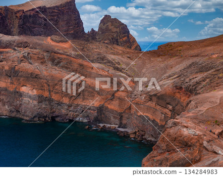 Jagged volcanic strata and eroded gullies meet deep cobalt water at Ponta de Sao Lourenco, Madeira, Portugal, under warm daylight from a slightly elevated view 134284983