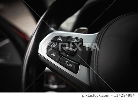 Detailed view of a BMW steering wheel with cruise control and driving assistance buttons, featuring a metallic finish in a modern car shop setting. Detailed view of a BMW steering wheel with cruise control and driving assistance buttons, featuring a metallic finish in a modern car shop setting. 134284994