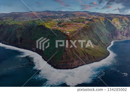 Aerial view of a sea cliff on Madeira near Ponta do Pargo or Sao Vicente, terraced fields and white farm buildings above Atlantic surf in soft late day light with long shadows. 134285002