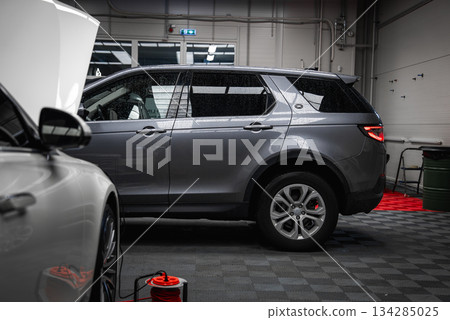 A gray Range Rover Discovery is parked in a well lit garage with tiled floors, white walls, overhead lighting, and a visible exit sign in the background. 134285025