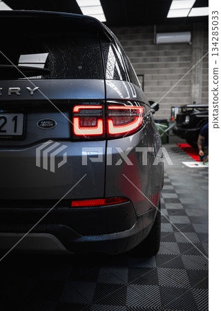 Silver Land Rover Discovery with illuminated taillights parked on checkered floor. Black Mercedes G Class and person working visible in background. 134285033