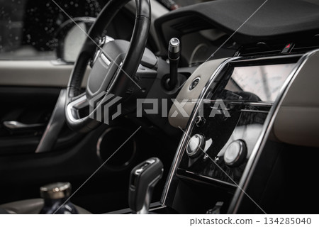 Luxury Range Rover Discovery interior featuring a sleek dashboard, touchscreen display, rotary dials, and premium materials in a showroom setting. Luxury Range Rover Discovery interior featuring a sleek dashboard, touchscreen display, rotary dials, and premium materials in a showroom setting. 134285040