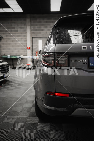 Silver Range Rover Discovery Sport with wet surface parked in a clean garage. Tiled floor, concrete wall, tools, and a partially visible vehicle present. Silver Range Rover Discovery Sport with wet surface parked in a clean garage. Tiled floor, concrete wall, tools, and a partially visible vehicle present. 134285042