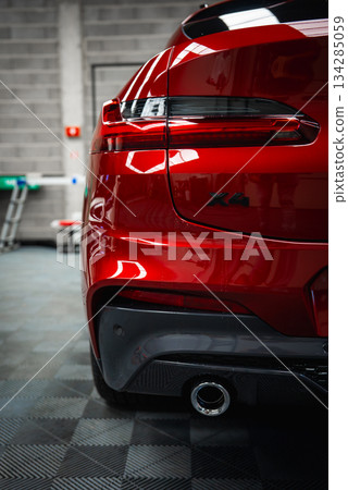 The rear section of a red BMW X4 with a visible model badge, parked in a clean garage with tiled floors, a gray brick wall, and industrial equipment. The rear section of a red BMW X4 with a visible model badge, parked in a clean garage with tiled floors, a gray brick wall, and industrial equipment. 134285059