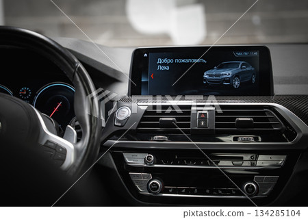 BMW dashboard featuring a central screen with a welcome message in Russian, glossy and textured materials, illuminated gauges, and a digital clock. 134285104