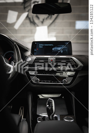 The BMW X4 interior features a modern dashboard with glossy black and metallic accents, an infotainment screen, and a gear selector in a car shop setting. 134285122