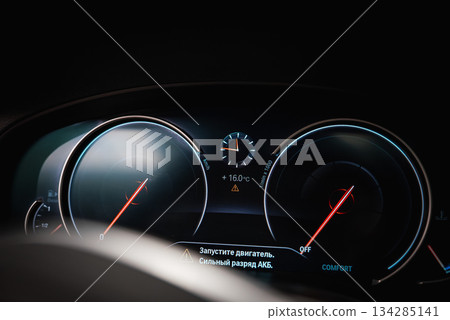 Close up of a BMW dashboard showing speedometer, tachometer, and digital display in Russian with engine start message and battery warning. 134285141
