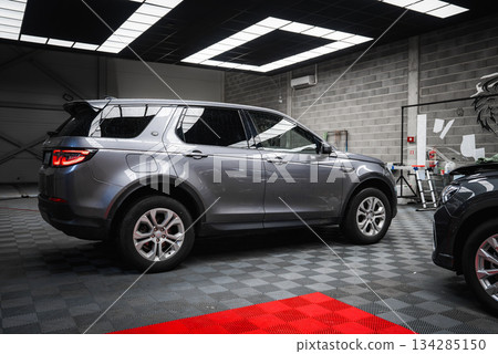 A silver Range Rover Discovery is parked in a well lit car shop garage with tiled floors, industrial walls, and tools visible in the background. 134285150