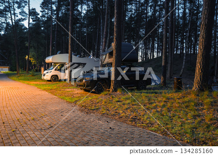 A black BMW X4 2025 with a rooftop tent is parked in a forested camping area. Warm lighting contrasts with twilight among tall pine trees and a camper van. A black BMW X4 2025 with a rooftop tent is parked in a forested camping area. Warm lighting contrasts with twilight among tall pine trees and a camper van. 134285160