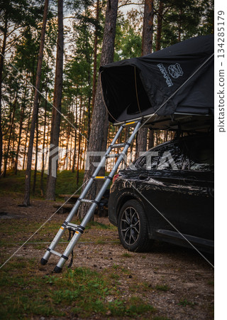 A black BMW X4 2025 parked in a forest, featuring an open rooftop tent with a ladder. Surrounded by tall pine trees and sunlight filtering through. A black BMW X4 2025 parked in a forest, featuring an open rooftop tent with a ladder. Surrounded by tall pine trees and sunlight filtering through. 134285179