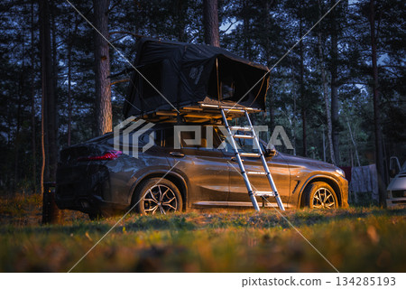 A BMW X4 2025 equipped with a rooftop tent is parked in a forested area during sunset. Tall trees surround the scene, with another vehicle in the background. A BMW X4 2025 equipped with a rooftop tent is parked in a forested area during sunset. Tall trees surround the scene, with another vehicle in the background. 134285193