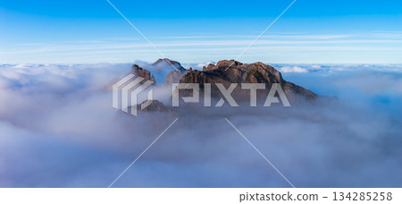 Dark rock spires rise above clouds at Pico do Arieiro in Madeira, Portugal. Wide panoramic view in soft light shows sharp ridgelines and smooth cloud layers. 134285258