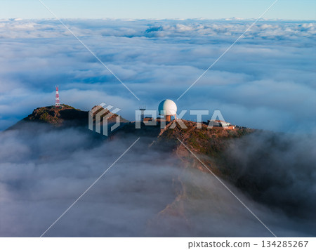 A large white geodesic radar dome and masts rise above clouds at Pico do Arieiro, Madeira, Portugal. Rugged red ridges, cool daylight, and haze suggest early or late day. A large white geodesic radar dome and masts rise above clouds at Pico do Arieiro, Madeira, Portugal. Rugged red ridges, cool daylight, and haze suggest early or late day. 134285267