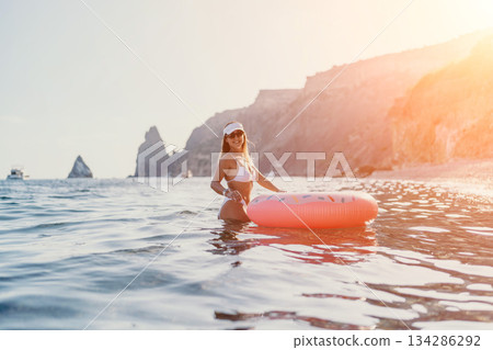 Woman, beach, ocean. Young woman in white bikini enjoys summer vacation with a donut float in the sea near cliffs, copy space. 134286292
