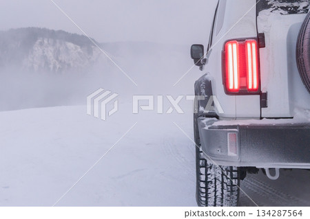 Snowy landscape with a white vehicle parked on a winter road in cold weather during a snowstorm. High quality photo 134287564