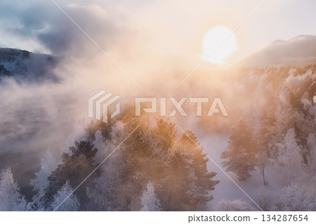 Sunlight breaks through misty clouds, reflecting on snowy trees in Krasnoyarsk, Russia, marking the New Year season in Siberia. Nature showcases its winter beauty in peaceful surroundings. High 134287654