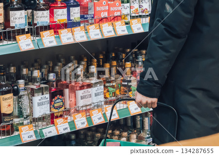 Krasnoyarsk, Russia, 02 02 2025: A male customer chooses strong alcohol in a supermarket window. Alcohol prices, excise tax, and the problem of alcoholism and alcohol dependence. Sales hours. High 134287655