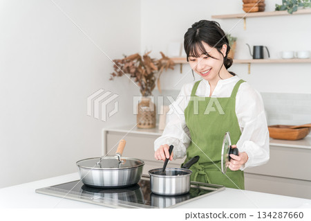 Young Asian woman in an apron cooking in the kitchen Young Asian woman in an apron cooking in the kitchen 134287660