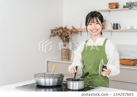 Young Asian woman in an apron cooking in the kitchen Young Asian woman in an apron cooking in the kitchen 134287663