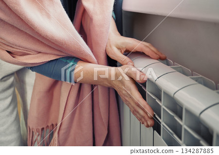 Woman feeling warmth from radiator, symbolizing comfort and heating during cold season 134287885