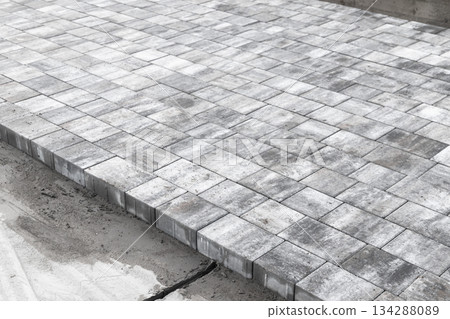 A level outdoor area made of square concrete paver tiles forms a modern walkway A level outdoor area made of square concrete paver tiles forms a modern walkway 134288089