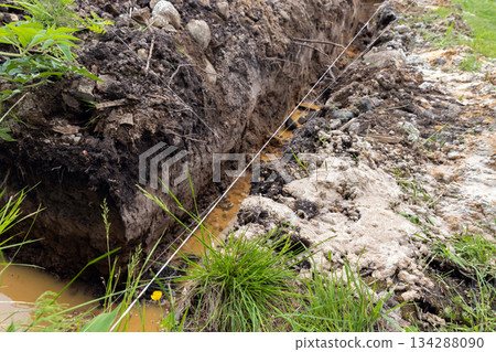 A trench filled with water surrounded by mud and grass 134288090