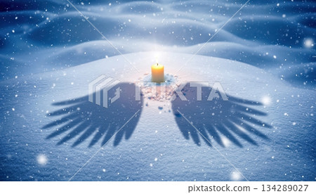 A single candle burns warmly in the snowy night as soft wing-shaped shadows stretch across the frozen ground, creating a magical winter moment filled with quiet beauty, calm light, and gentle wonder 134289027