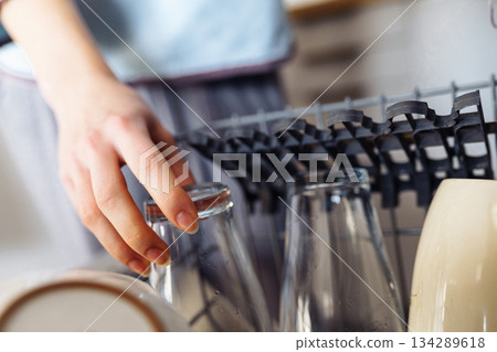 young woman putting dirty dishes into dishwasher at home 134289618