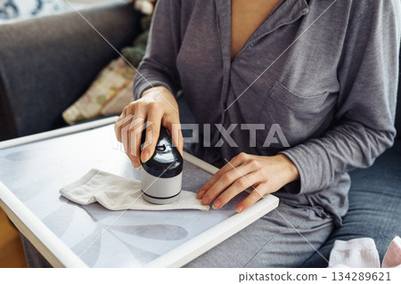 woman takes care of clothes at home, cuts off lint with tool 134289621