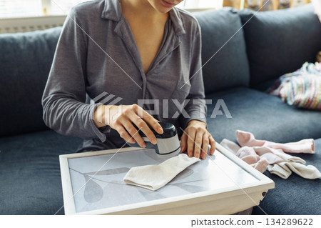 woman takes care of clothes at home, cuts off lint with tool 134289622