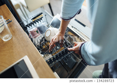 young woman putting dirty dishes into dishwasher at home 134289723
