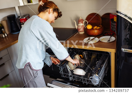 young woman putting dirty dishes into dishwasher at home young woman putting dirty dishes into dishwasher at home 134289737