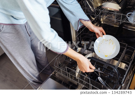 young woman putting dirty dishes into dishwasher at home 134289743
