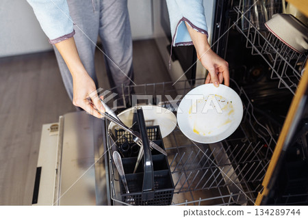 young woman putting dirty dishes into dishwasher at home young woman putting dirty dishes into dishwasher at home 134289744