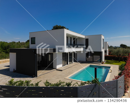 Modern luxury villa with swimming pool and clean minimalist architecture under a blue sky. Contemporary residential exterior featuring large windows, terrace, and elegant outdoor living space 134290436