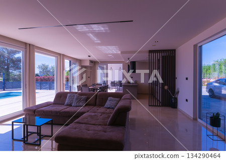 Modern open-plan living and dining room in a luxury villa with large glass doors opening to a private swimming pool, offering a spacious and elegant indoor-outdoor living experience 134290464