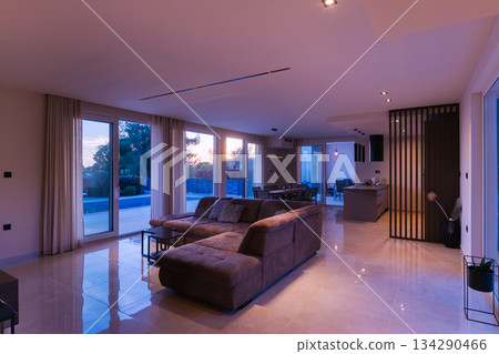 Modern, bright living room featuring a comfortable sofa and panoramic glass doors opening to a stunning private swimming pool and lush garden. Perfect for luxurious indoor-outdoor living Modern, bright living room featuring a comfortable sofa and panoramic glass doors opening to a stunning private swimming pool and lush garden. Perfect for luxurious indoor-outdoor living 134290466