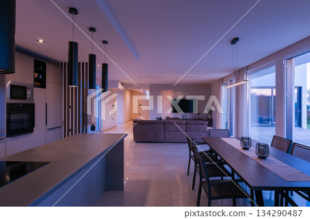 Modern, bright living room featuring a comfortable sofa and panoramic glass doors opening to a stunning private swimming pool and lush garden. Perfect for luxurious indoor-outdoor living 134290487