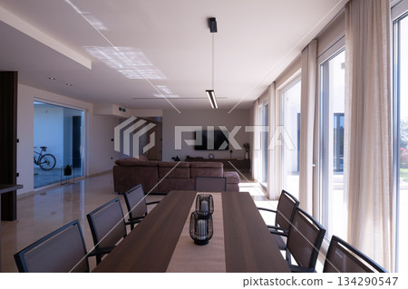 Modern open-plan living and dining room in a luxury villa with large glass doors opening to a private swimming pool, offering a spacious and elegant indoor-outdoor living experience Modern open-plan living and dining room in a luxury villa with large glass doors opening to a private swimming pool, offering a spacious and elegant indoor-outdoor living experience 134290547