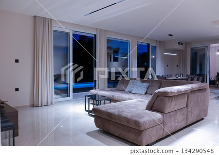 Modern, bright living room featuring a comfortable sofa and panoramic glass doors opening to a stunning private swimming pool and lush garden. Perfect for luxurious indoor-outdoor living Modern, bright living room featuring a comfortable sofa and panoramic glass doors opening to a stunning private swimming pool and lush garden. Perfect for luxurious indoor-outdoor living 134290548